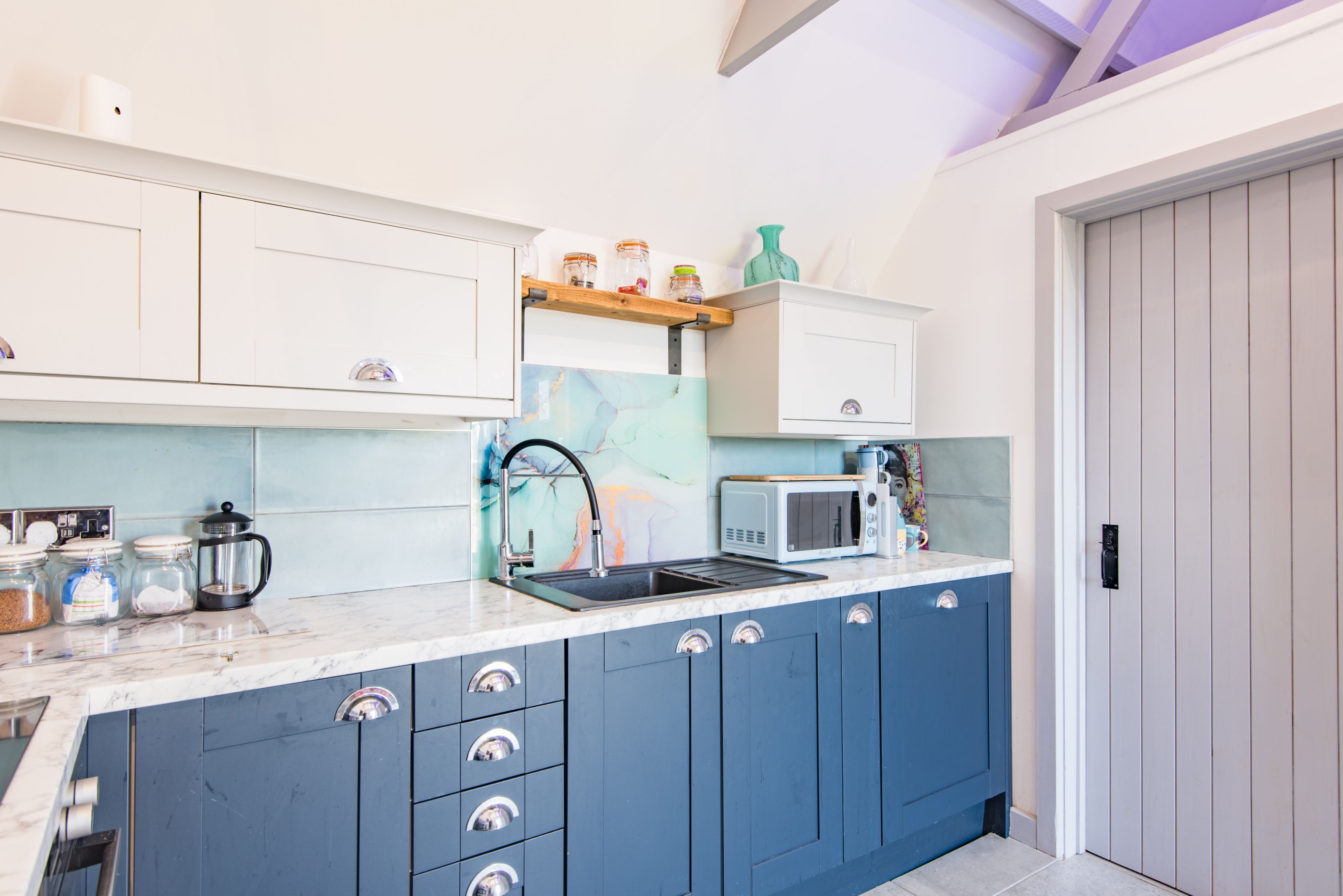 A modern kitchen with blue cabinets, a marble countertop, a coffee maker, and a microwave.