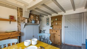 Un comedor con una mesa de madera dispuesta para cuatro personas, una silla azul y una cocina rústica al fondo.