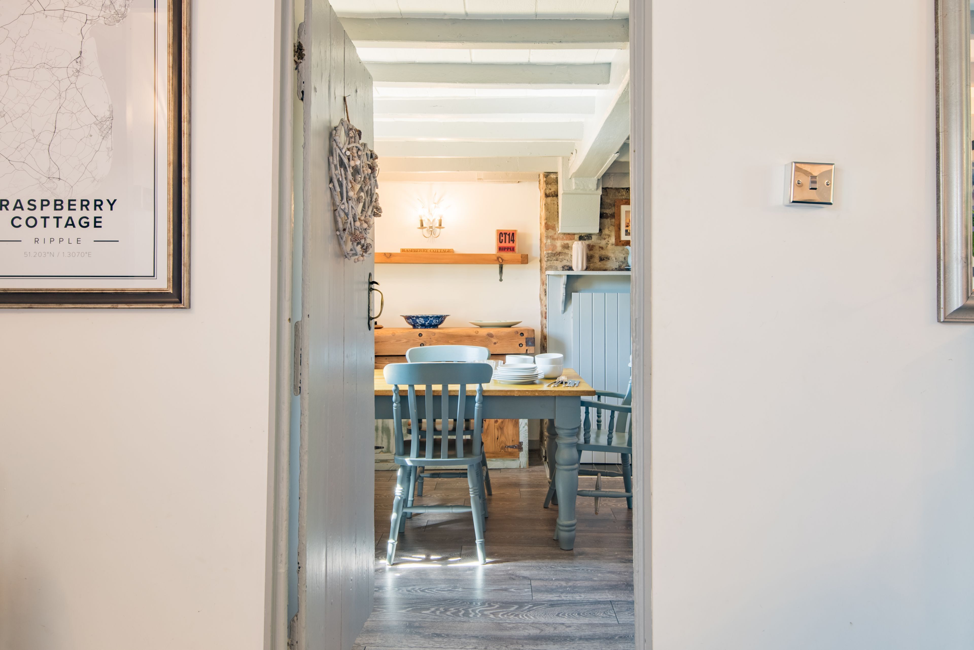 A dining area with a wooden table and blue chairs, a map on the wall, and a kitchen in the background.