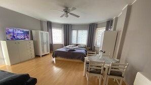 A bedroom with a bed, a desk with chairs, a television, and a ceiling fan.