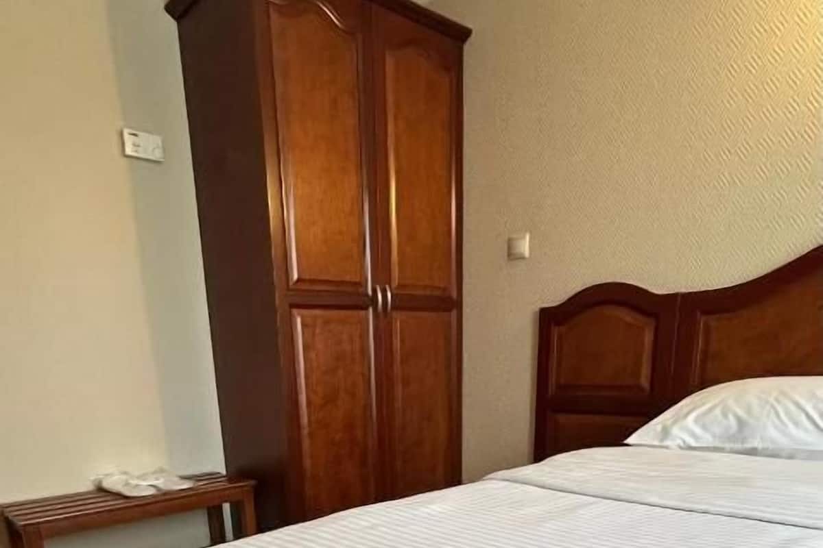 A hotel room with a large bed, wooden wardrobe, and a small bedside table.