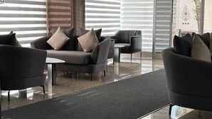 Un moderno vestíbulo con área de descanso, un panel de madera decorativo y un ventanal con persianas.