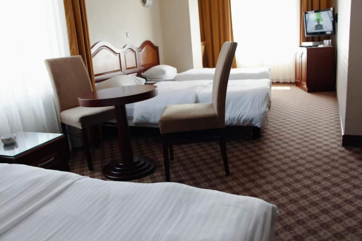 A hotel room with two beds, a desk, a chair, a television, and a carpeted floor.