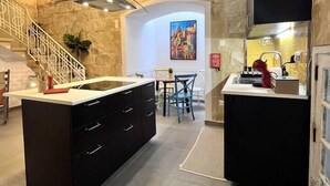 Una cocina moderna con una isla central, un comedor con sillas y una escalera que sube a un nivel superior.