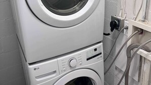 Un appareil combiné lave-linge et sèche-linge, de type « empilable », doté de panneaux de commande et de tuyauterie visible.