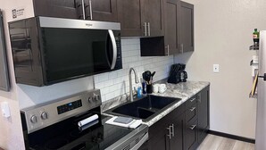 Une cuisine moderne avec des meubles de couleur sombre, un four à micro-ondes encastré, une cuisinière en acier inoxydable, un évier et une machine à café.