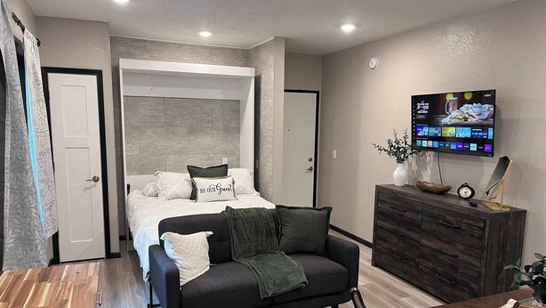Une chambre à coucher moderne avec un lit, un canapé, une télévision et une commode en bois.