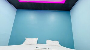 Un dormitorio con cama, ventilador de techo e iluminación rosada en el techo.
