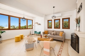 A spacious living room with large windows, a sofa, a coffee table, and a fireplace.