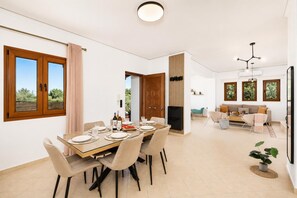 A modern living space with a dining area, sofa, TV, and large windows.