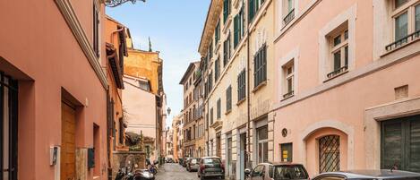 A narrow cobblestone street lined with historic buildings, parked cars, and motorcycles.