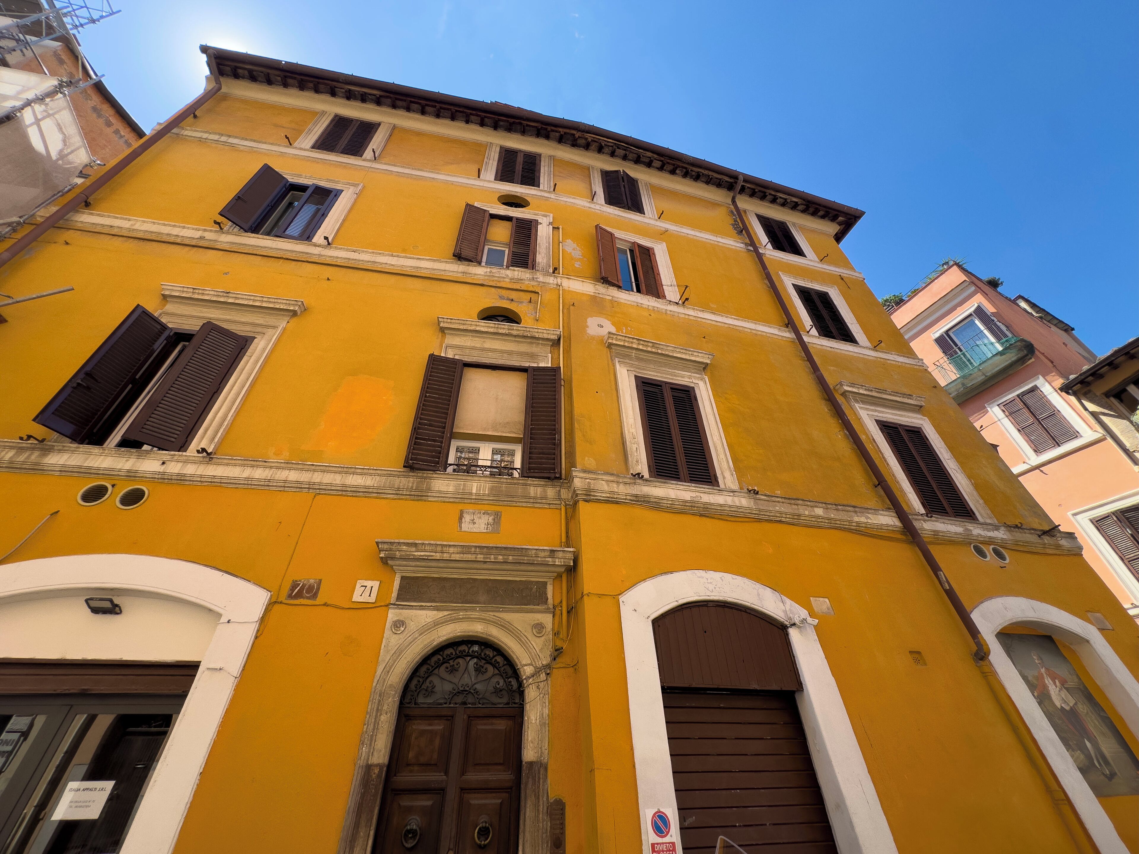 A yellow building with a brown door and windows, featuring a number '71' sign.