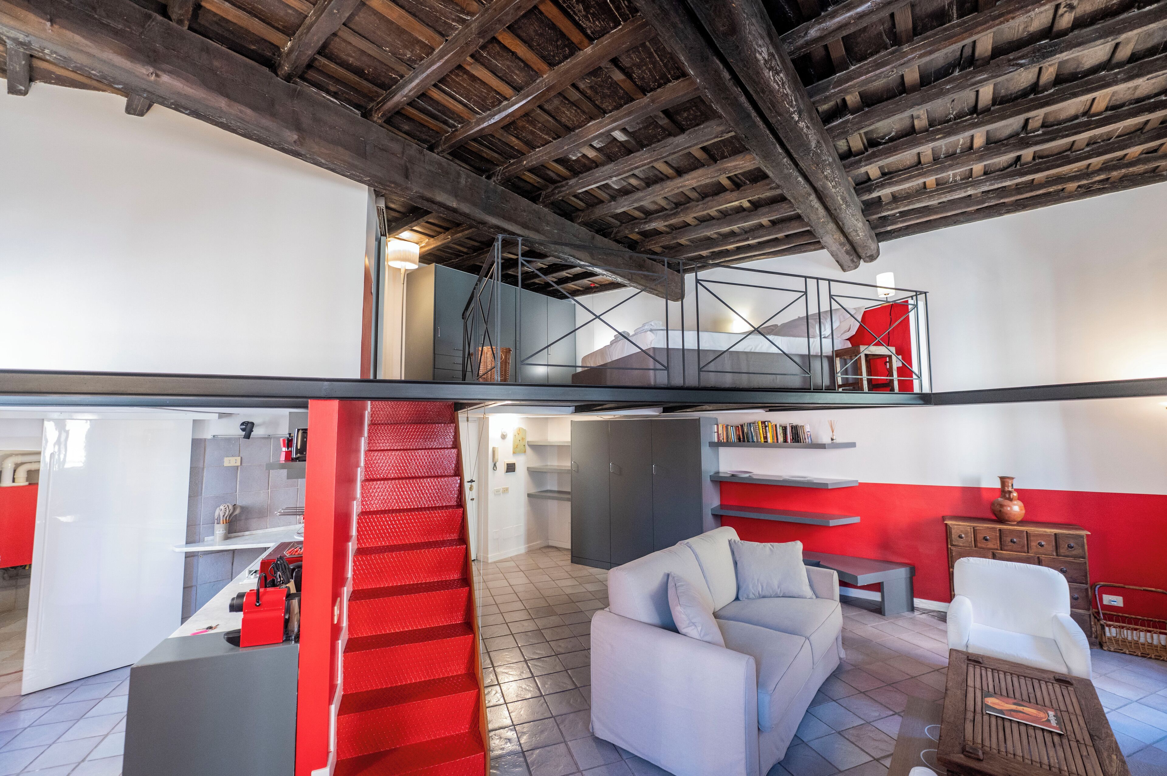 A spacious living area with a staircase leading to an upper level, a kitchen area, and a seating area with a red accent wall.