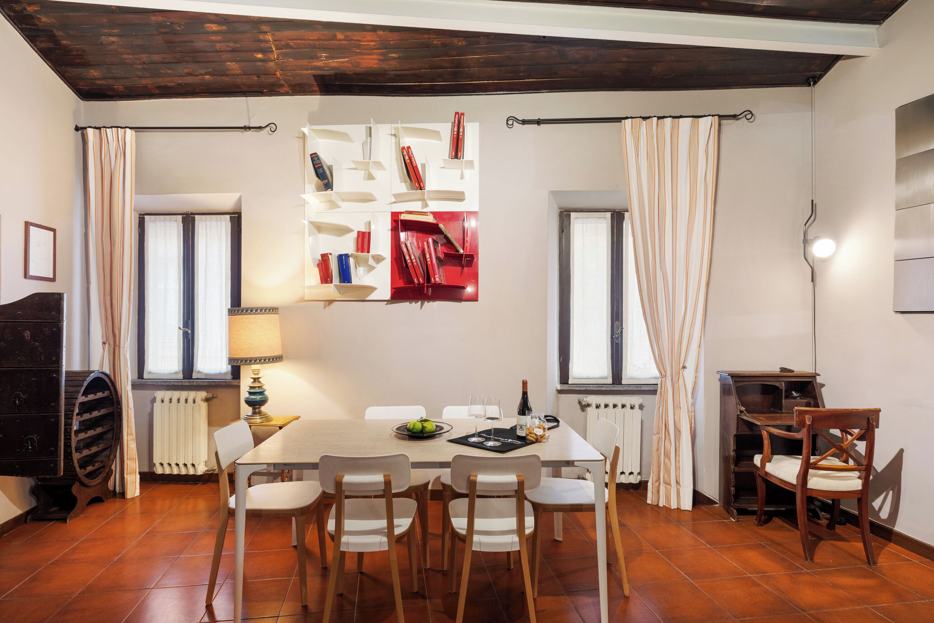 Un coin repas avec une table dressée pour quatre personnes, entourée de chaises, une bibliothèque remplie de livres et un radiateur.