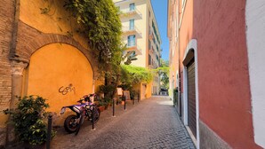Un carrer empedrat estret amb una motocicleta aparcada, una paret groga amb graffitis i un edifici amb façana vermella i blanca.