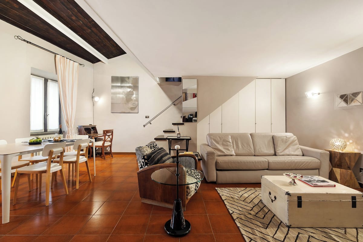 Una sala de estar moderna con comedor, un sofá, una mesa de centro y una escalera que sube a un nivel superior.
