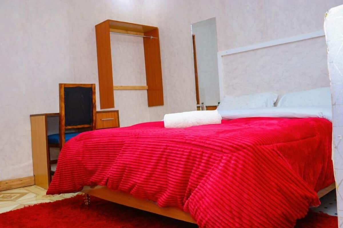Une chambre à coucher avec un lit, une armoire en bois, un miroir et un tapis rouge.