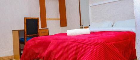 Un dormitorio con cama, un armario de madera, un espejo y un tapete rojo.