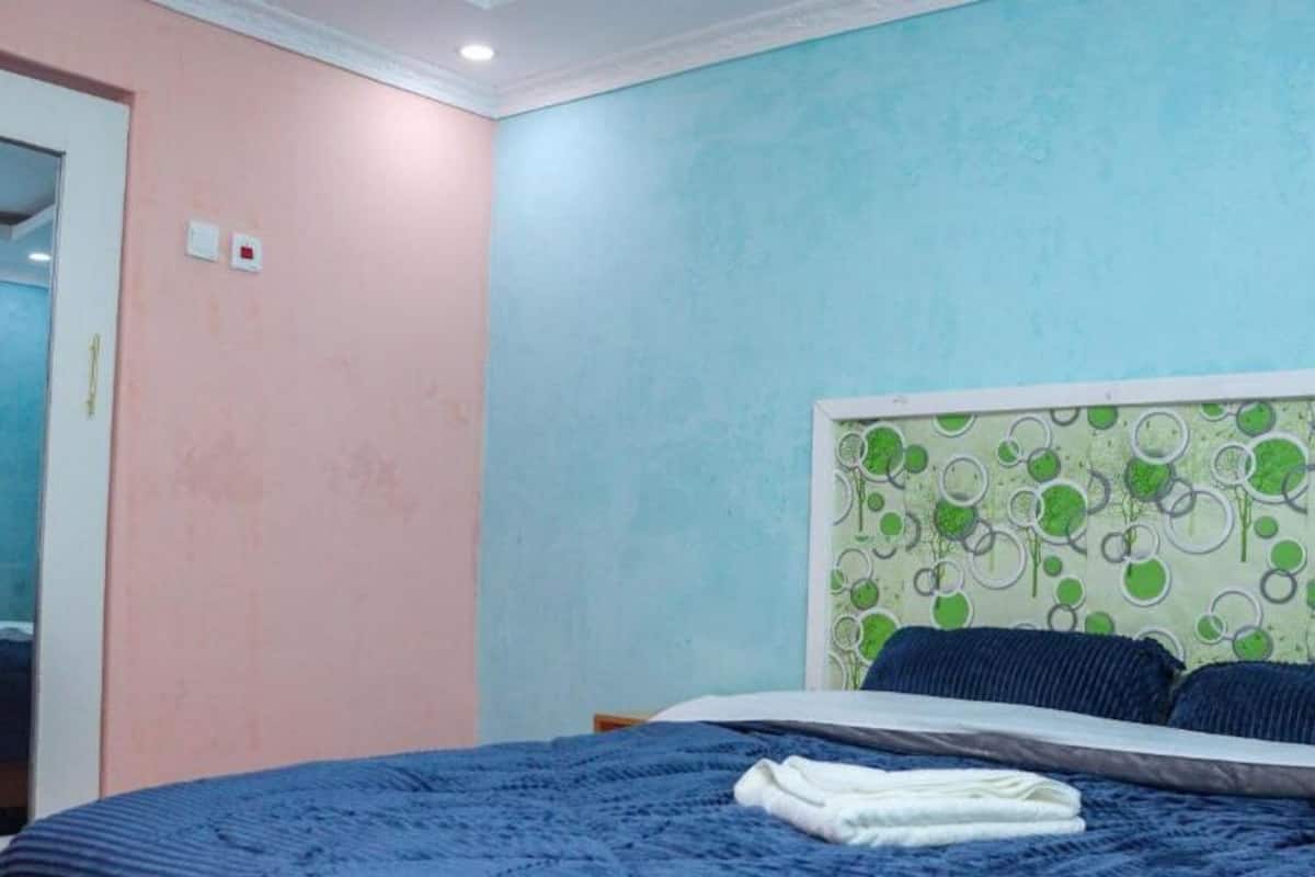 Une chambre à coucher avec un lit, une tête de lit à motifs verts et blancs, et un mur rose.