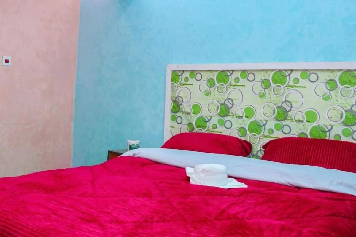 Une chambre à coucher avec un lit, une tête de lit à motifs verts et blancs, et un mur bleu clair.