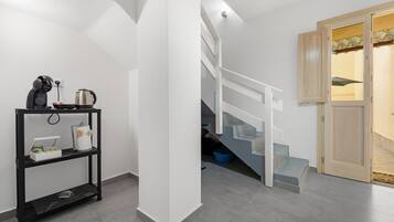Un escalier menant à un deuxième étage, une étagère en métal noir contenant des ustensiles de cuisine et une porte en bois donnant sur un paysage agréable.