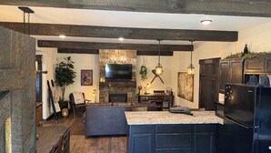 A modern kitchen with a large island, dark cabinetry, and a stone fireplace. - The Ancient Bear’s Den of the Forgotten Forest (Kodak)