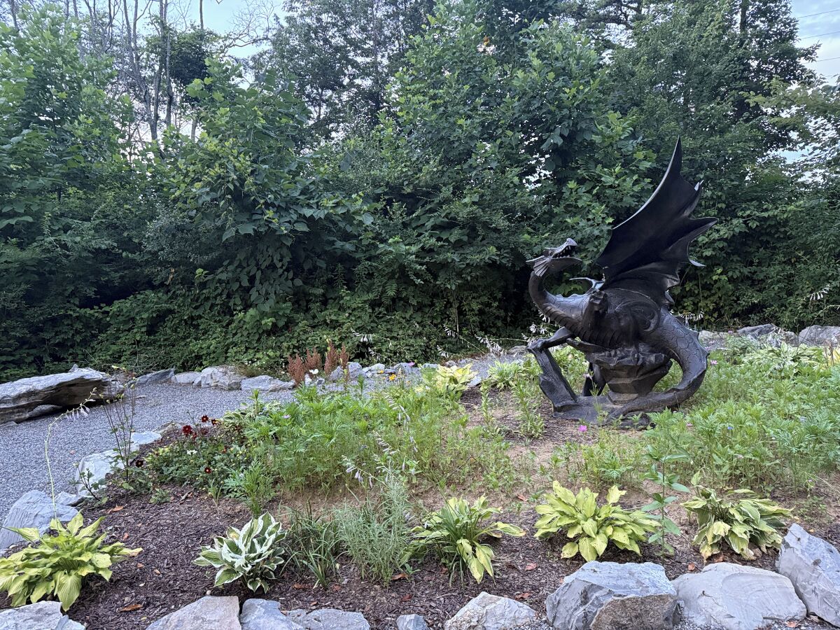 A garden with a statue of a winged creature, surrounded by various plants and rocks.