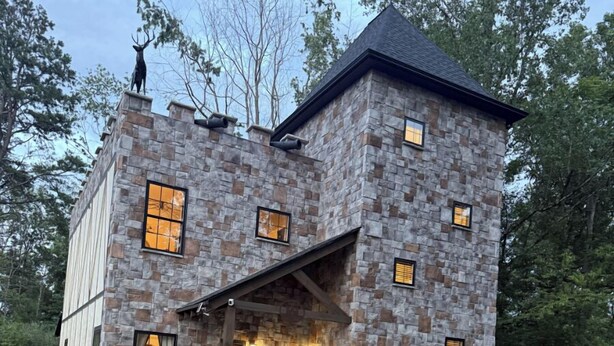 A stone house with a stone chimney, a porch with a statue, and a deer statue on the roof. - The Ancient Bear’s Den of the Forgotten Forest (Kodak)