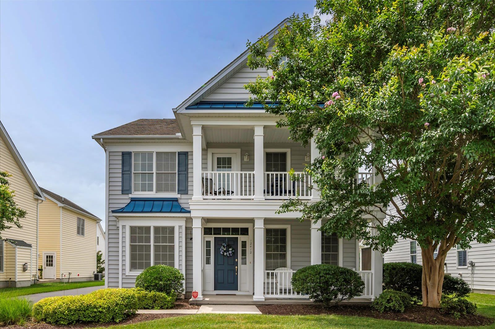 A two-story house with a front porch, a small front yard, and a tree.