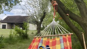 En hängmatta som hänger mellan träd på en gräsyta, med en byggnad i bakgrunden.
