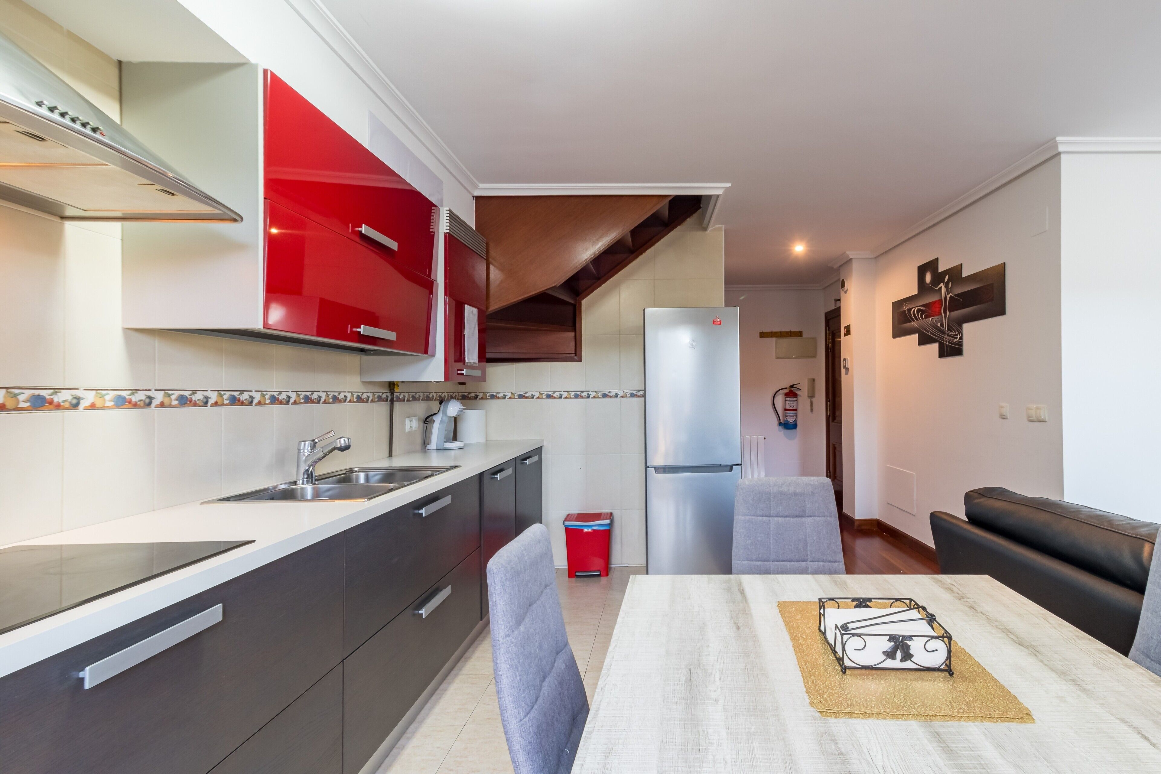 A modern kitchen with red cabinets, a stainless steel refrigerator, and a dining area with a table and chairs.