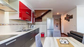 A modern kitchen with red cabinets, a stainless steel refrigerator, and a dining area with a table and chairs.