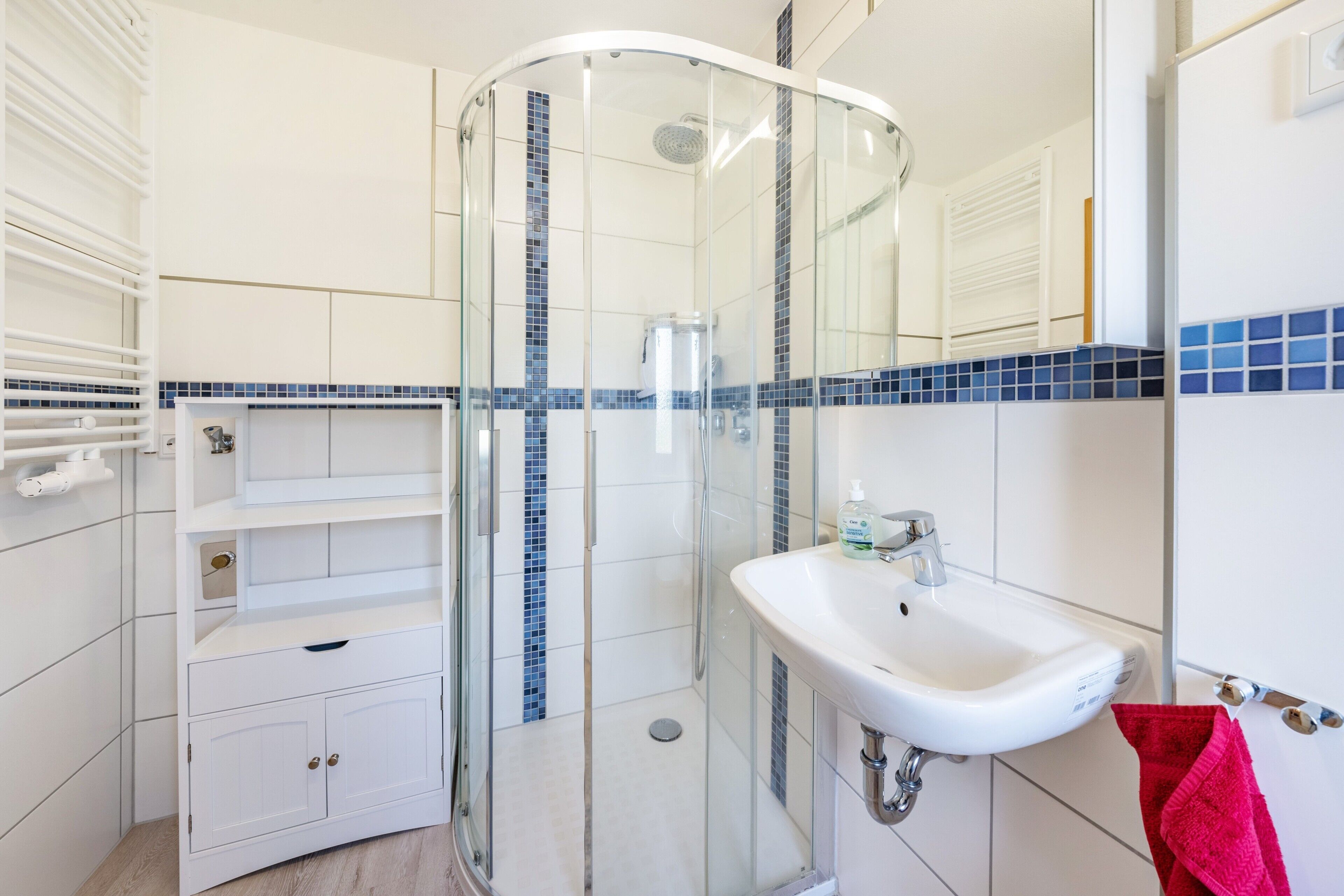 Ein modernes Badezimmer mit einer Duschkabine aus Glas, einem weißen Waschbecken und einer gefliesten Rückwand.