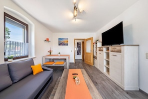 A modern living room with a sofa, a dining table, a TV, and a wooden cabinet.
