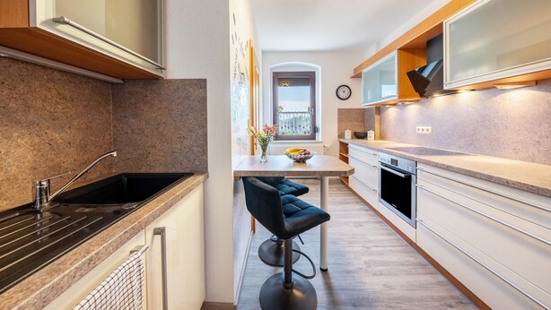 A modern kitchen with a built-in oven, a sink, and a bar stool.