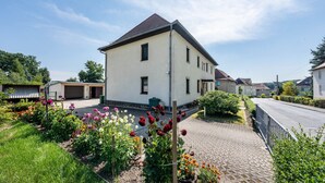 A residential house with a paved driveway, a garage, and a garden with various flowers.