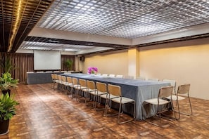 Uma sala de conferências com uma mesa comprida, cadeiras e tela de projeção.