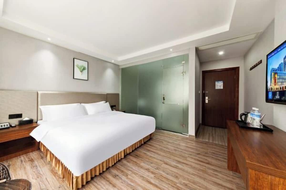 A hotel room with a large bed, a desk, a television, and a door leading to another room.