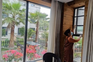 Una persona limpiando una ventana en una habitación con vista a un jardín y un balcón.