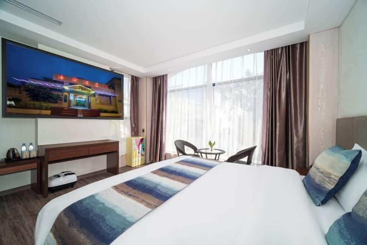 A hotel room with a large bed, a TV mounted on the wall, a desk, and a chair.