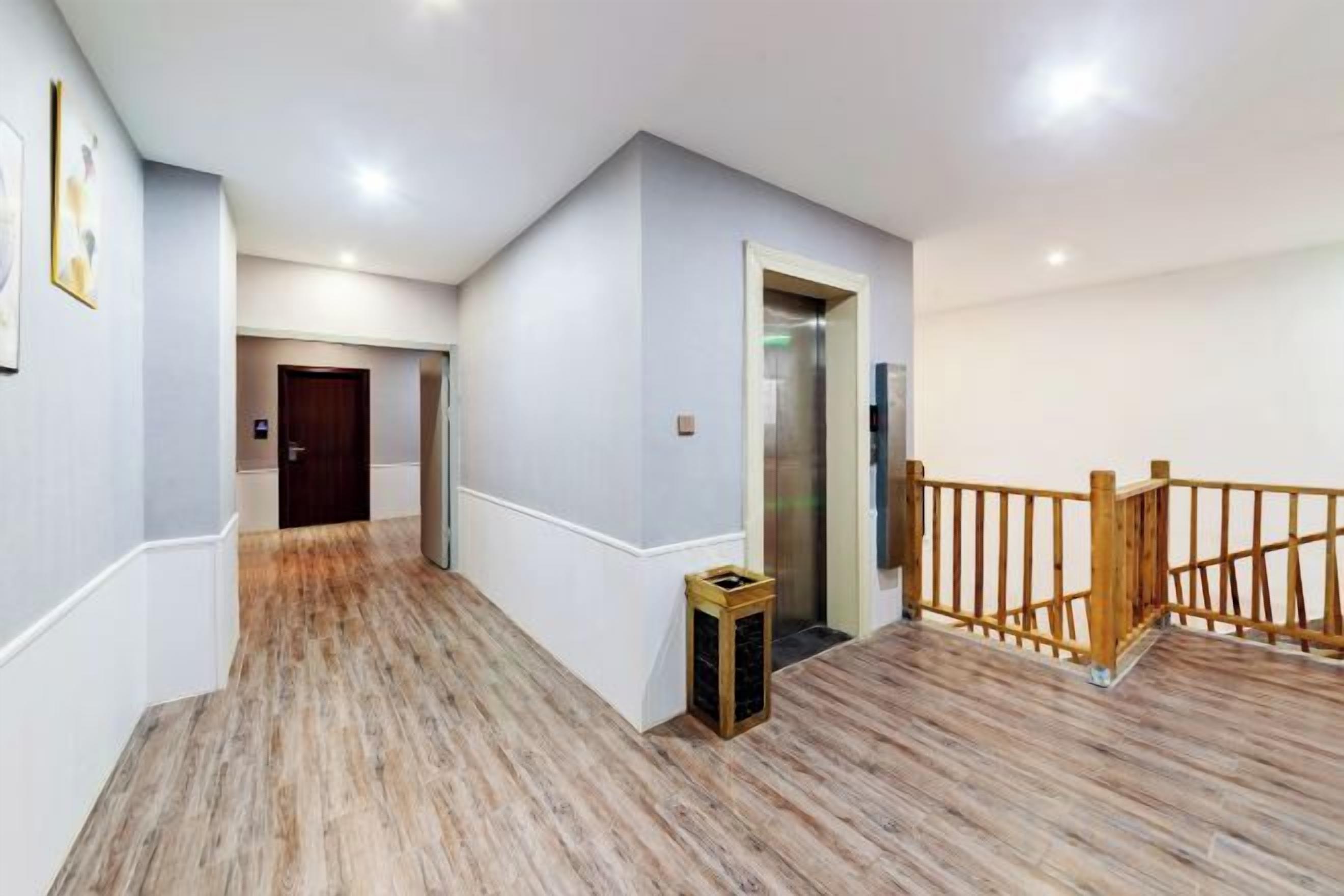 A hallway with wooden flooring, a wooden railing, and a door leading to an elevator.