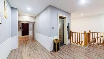 A hallway with wooden flooring, a wooden railing, and a door leading to an elevator.