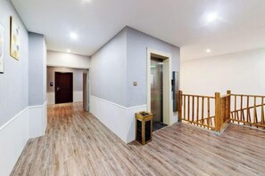 Un corridoio con pavimento in legno, ringhiera in legno e una porta che dà sull'ascensore.