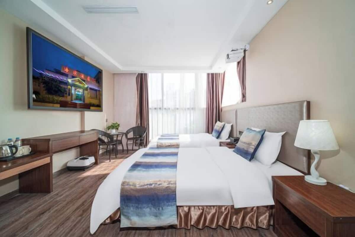 A hotel room with a bed, bedside tables, a desk, a chair, and a large window.