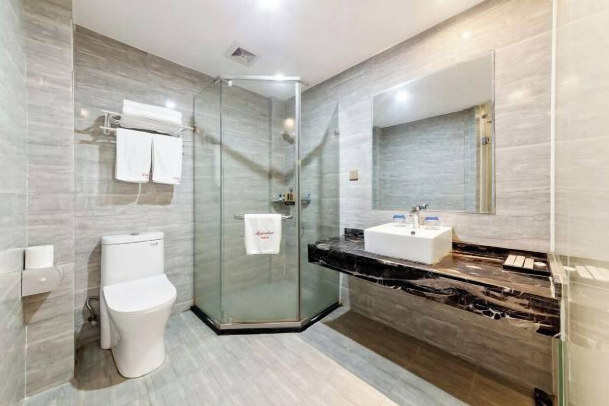 A modern bathroom with a glass shower enclosure, a white toilet, a marble countertop, and a large mirror.