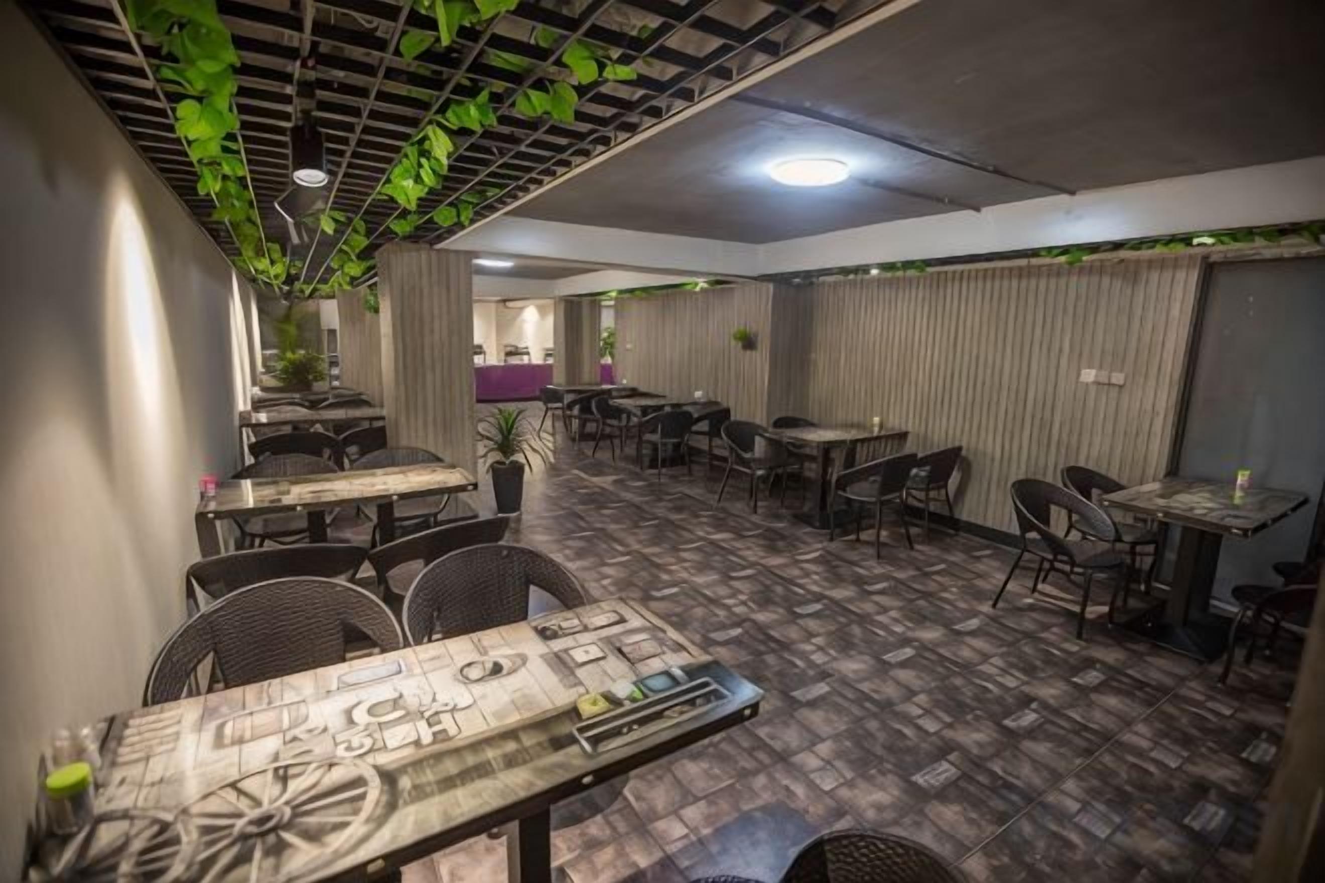 An indoor dining area with tables and chairs, a patterned floor, and a ceiling with hanging greenery.