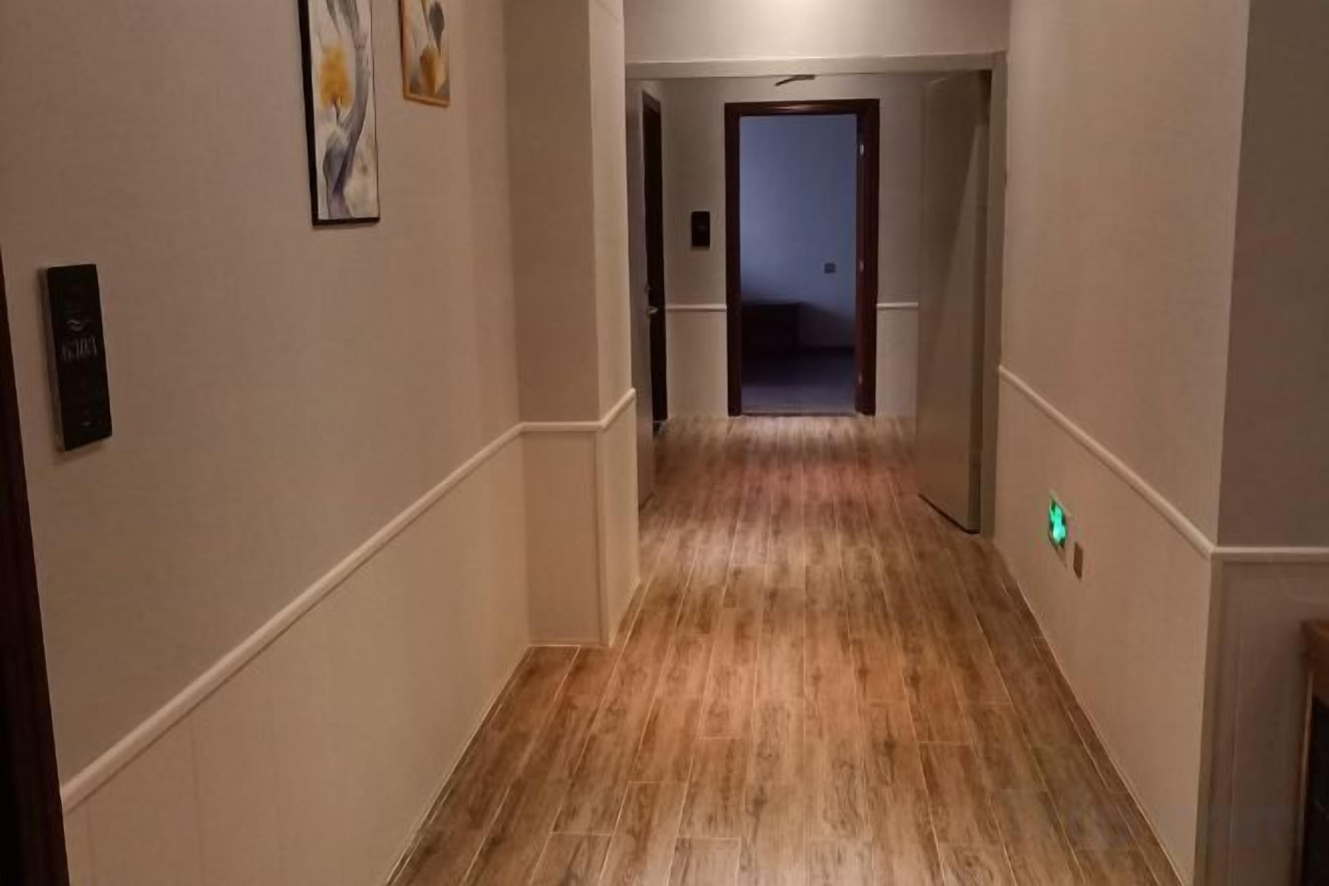A hallway with a wooden floor, white walls, and a door at the end.
