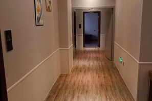 Un corridoio con pavimento in legno, pareti bianche e una porta in fondo.