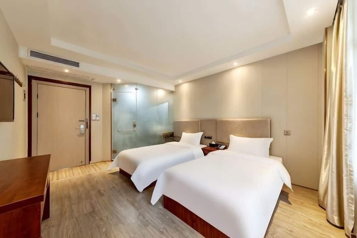 A hotel room with two beds, a desk, a mirror, and a door.