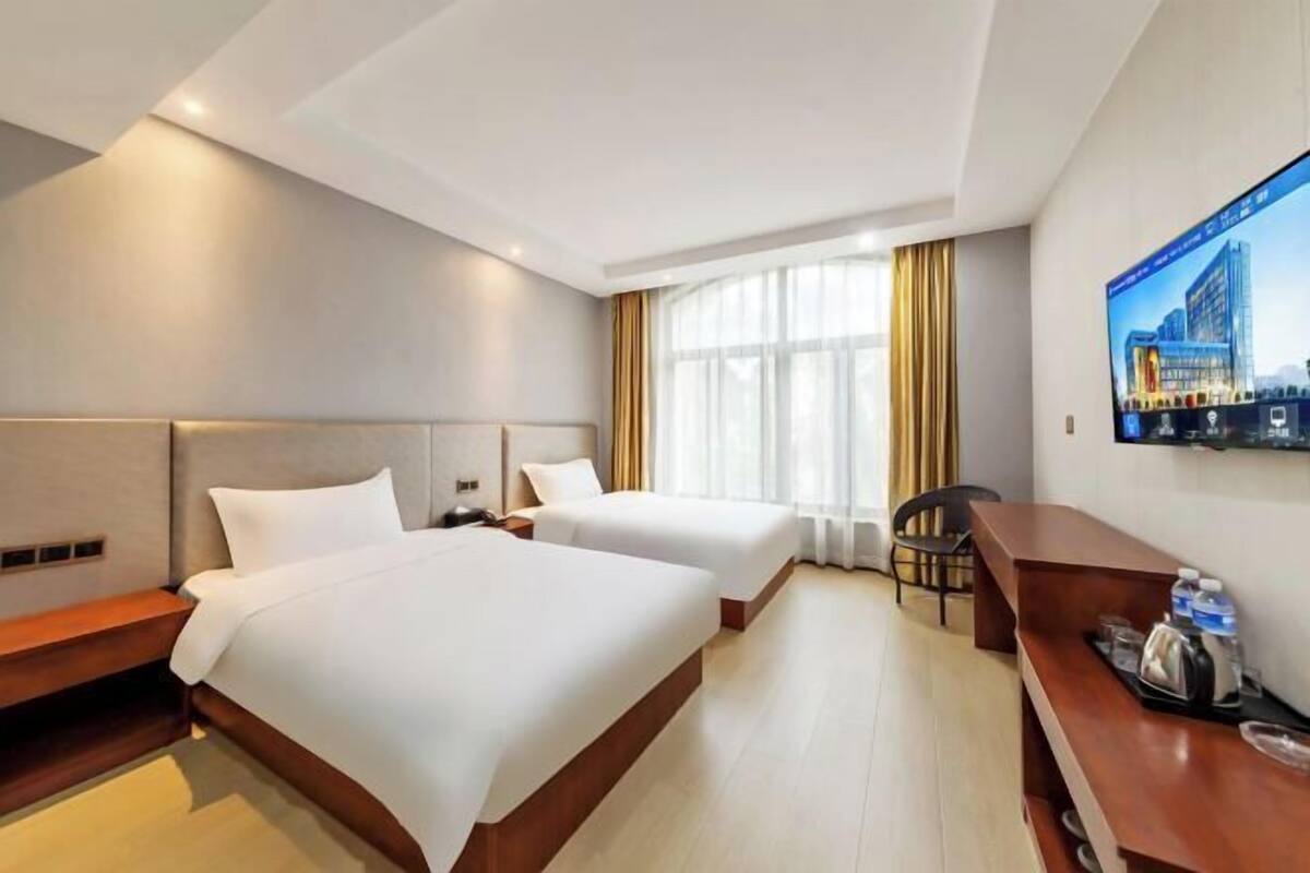 A hotel room with two beds, a desk, a chair, a TV, and a window with curtains.